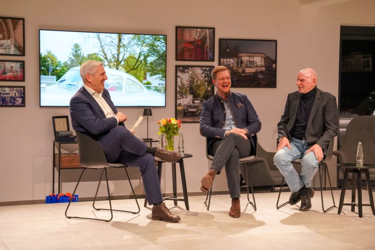Zu sehen ist Herr Genz bei einer Podiumsbesprechung mit zwei weiteren Personen.