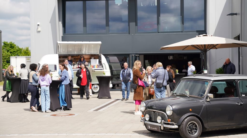 Auf dem Bild wir ein Fest vor dem Gebäude von Wallner Classic gezeigt. Es sind einige Personen zu sehen die Getränke in der Hand halten.