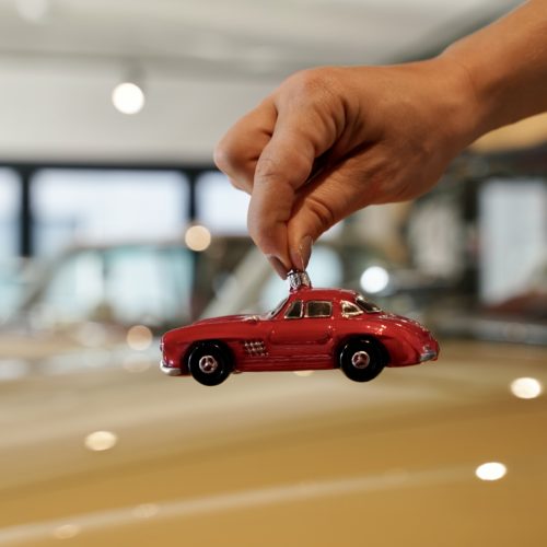 Zu sehen ist eine Hand, die eine rot Christbaumkugel in Forma eines Oldtimer Fahrzeugs hält.