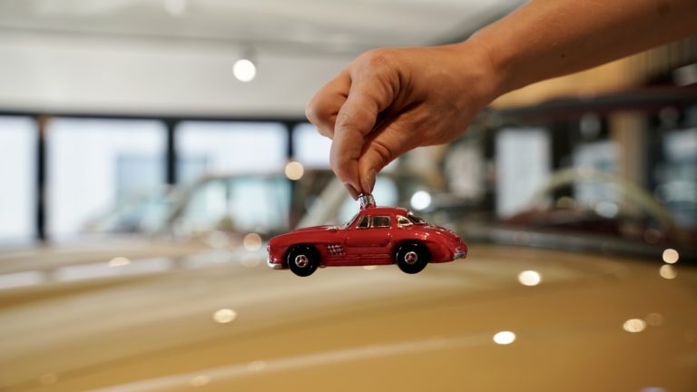 Zu sehen ist eine Hand, die eine rot Christbaumkugel in Forma eines Oldtimer Fahrzeugs hält.