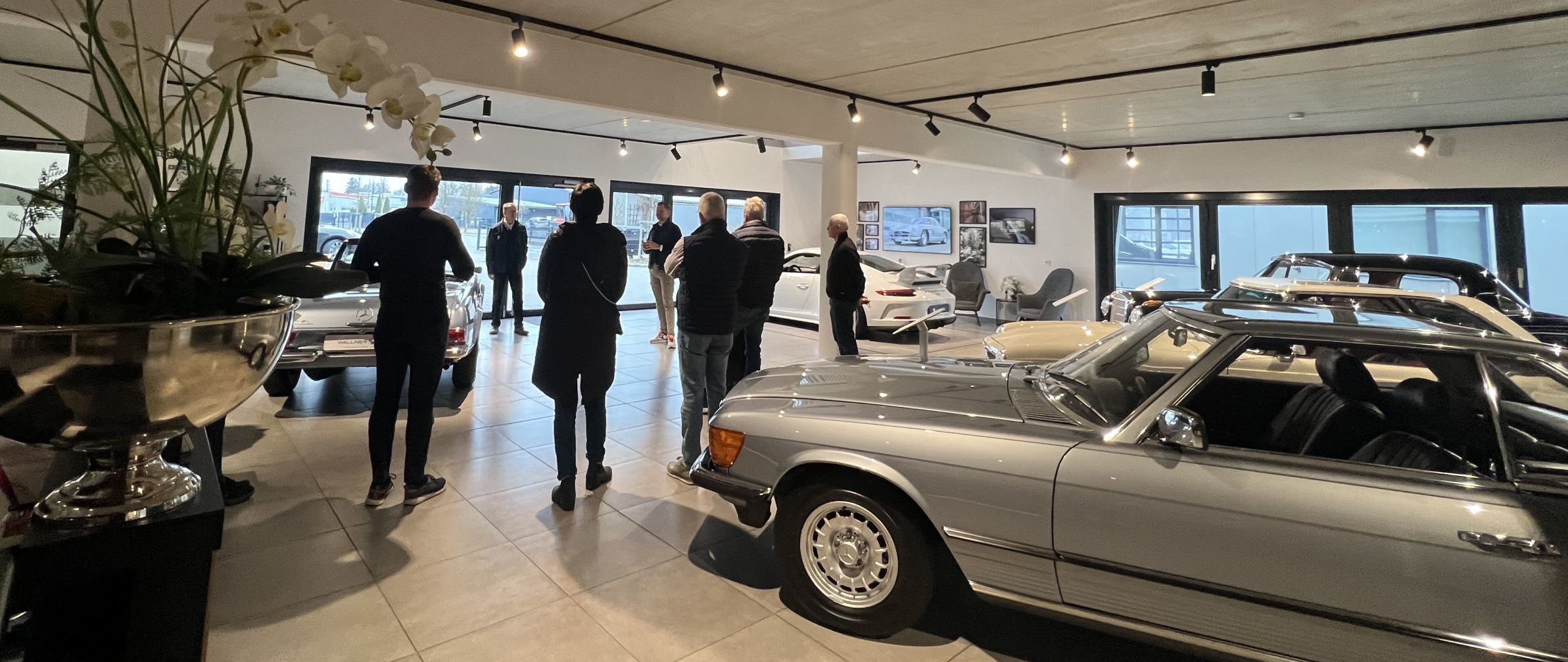 Zu sehen ist ein Ausstellungsraum mit mehreren Mercedes Fahrzeugen und Kunden in einem Halbkreis aufgestellt.